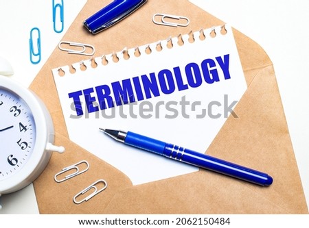 On a light background, a craft envelope, an alarm clock, paper clips, a blue pen and a sheet of paper with the text TERMINOLOGY