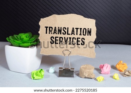 On a light background, gold-framed glasses, a flower in a pot, a green notebook, a red pen and a brown notebook with the text TRANSLATION SERVICES. Business concept