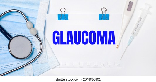 On A Light Background Lie A Stethoscope, An Electronic Thermometer, A Syringe, A Face Mask And A Sheet Of Paper With The Text GLAUCOMA. Medical Concept