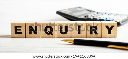 On a light background, a pen, calculator and wooden cubes with the inscription ENQUIRY. Defocus