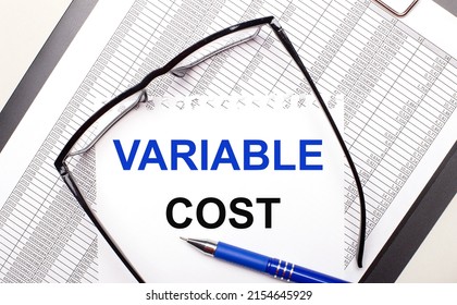 On a light background, a report, black-framed glasses, a pen and a sheet of paper with the text VARIABLE COST. Business concept