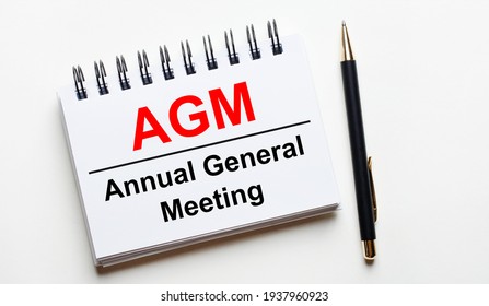 On a light background, a white notebook with are words AGM Annual General Meeting and a pen. - Shutterstock ID 1937960923