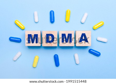 On a light blue background, multicolored pills and wooden cubes with the text MDMA. Medical concept