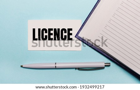 On a light blue background, an open notebook, a white pen and a card with the text LICENCE. View from above