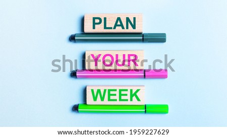 On a light blue background, there are three multi-colored felt-tip pens and wooden blocks with the PLAN YOUR WEEK text.