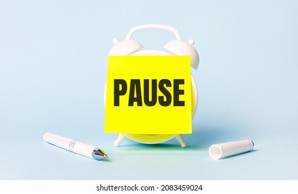 On a light blue background - a white handle and an alarm clock with a bright yellow sticker glued to it with the text PAUSE - Shutterstock ID 2083459024