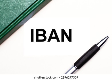 On A Light Gray Background Lies A Pen, A Green Notebook And A White Card With The Text IBAN International Bank Account Number. Business Concept.