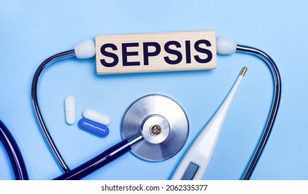 On a light gray background, a stethoscope, an electronic thermometer, pills, a wooden block with the text SEPSIS. Medical concept.