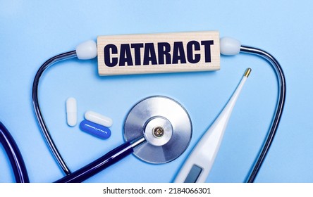 On A Light Gray Background, A Stethoscope, An Electronic Thermometer, Pills, A Wooden Block With The Text CATARACT. Medical Concept.