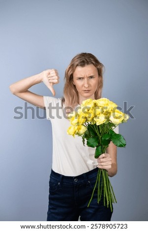 on light gray background a young blonde girl with a large yellow peony roses women's holiday March 8 emotions of discontent and confusion flowers for separation anger on face and thumb down