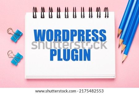 On a light pink background, light blue pencils, paper clips and a white notebook with the text WORD PRESS PLUGIN
