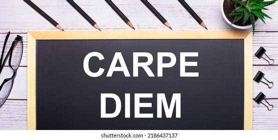 On a light wooden table - a board with the text CARPE DIEM, pencils, plants, glasses and paper clips. Business concept