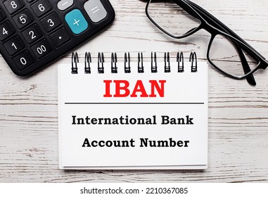 On A Light Wooden Table Calculator, Glasses And A Blank Notepad With The Text IBAN International Bank Account Number. Business Concept