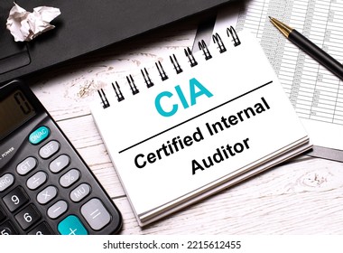 On A Light-colored Office Table Is A Computer, A Black Calculator, A Pen, And A Notebook With The Text CIA Certified Internal Auditor