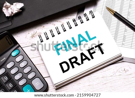 On a light-colored office table is a computer, a black calculator, a pen, and a notebook with the text FINAL DRAFT. Business concept.