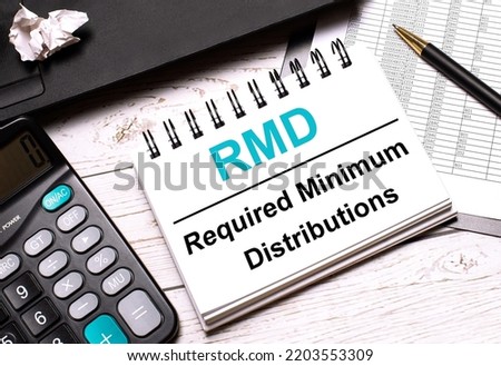 On a light-colored office table is a computer, a black calculator, a pen, and a notebook with the text RMD Required Minimum Distributions