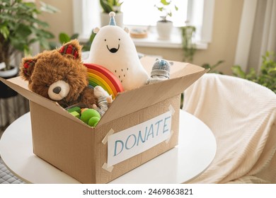 On the living room couch is a box full of toys for donation. Teddy bear soft toy, colored wooden cubes, cars. Donat concept.