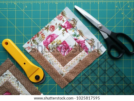  On the mat for patchwork sewing there are scissors, a knife for patchwork, a ruler, a patchwork napkin  