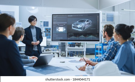 On A Meeting Asian Specialist Reports To A Group Of Engineers, Managers, Presents New Electrical Car Concept, Using Digital Whiteboard. Electric Car Development, Factory.