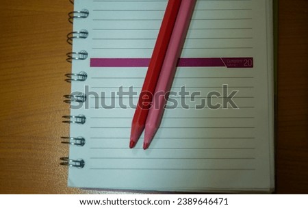 On a notepad, two distinct tones of pink pencils create a visually appealing contrast, adding a touch of creative vibrancy and organization to the workspace.