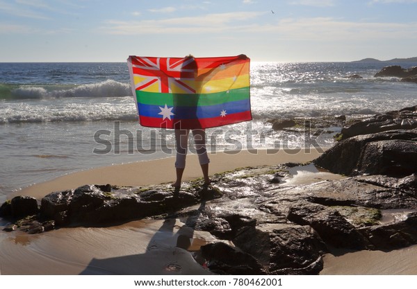 On November 15 Australia voted yes to Marriage\
Equality.  A woman holding an Australian flag in rainbow colours by\
the ocean