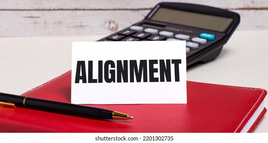 On The Office Desk There Is A Burgundy Notebook, A Calculator, A Pen And A White Card With The Text ALIGNMENT. Business Concept.