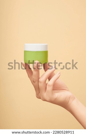 On the palm of the woman's hand is a moisturizing cream made of green glass on a beige background. Unlabeled bottle mockup of anti-aging masks, exfoliating cosmetics. Skin care concept