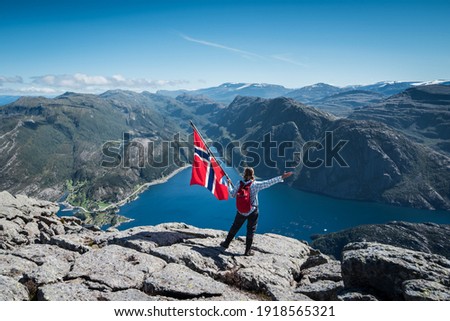 On the peak of scenic Hornelen Europe's Highest Sea Cliff with female model waving a Norwegian Flag 