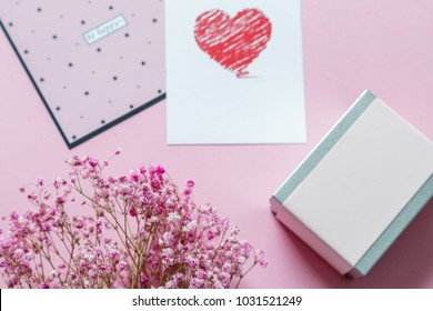 on a pink background flat lie: a gift box, a bouquet of flowers and cards with the inscriptions 