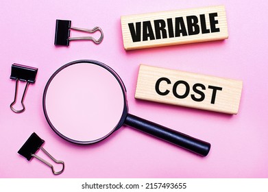 On a pink background, a magnifier, black paper clips and wooden blocks with the text VARIABLE COST. Business concept