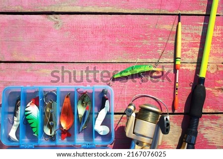 On a pink wooden background, close-up of a fishing rod, float, fishing line, reel, baubles in a box, a wobbler on a fishing line.Fishing tackle on a wooden pier, place for text