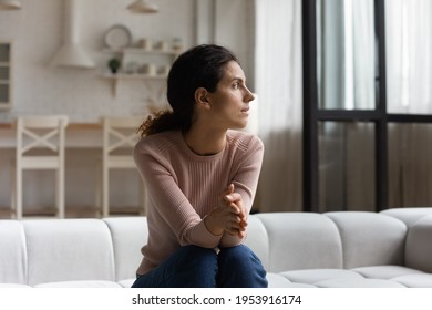 On pins and needles. Worried hispanic woman sit on couch at home hold hands together look aside expect for important guest. Nervous young latin female troubled with job interview result wait for call - Shutterstock ID 1953916174