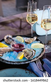on a plate are four oysters, slices of lemon and blue ice. next are two glasses of champagne