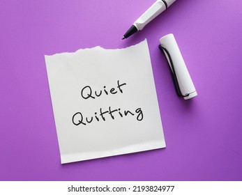 On purple background, pen writing on paper note QUIET QUITTING, when employees not engaged or taking job seriously, do minimum required but focus on job outside office