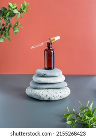 On the pyramid of stones is an open glass brown bottle with a pipette. Oil is dripping from the pipette. Skin care concept. Natural ingredients. Copy space. Vertical. 
Brown gray background.
Side view