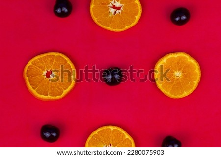 On a red background are circles of cut juicy orange and ripe cherries. A beautiful combination of orange and cherry on a rich red background. Fruits and berries are rich in vitamins.