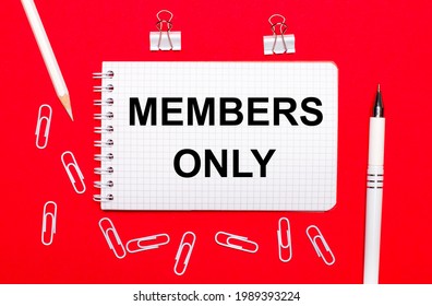 On A Red Background, A White Pen, White Paper Clips, A White Pencil And A Notebook With The Text MEMBERS ONLY. View From Above