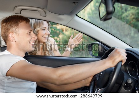 On the road. Portrait of a handsome young man driving a car and asking a road while a beautiful young blond girl with curvy hair showing him a route, both smiling