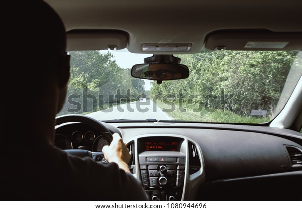 On the road - unrecognizable person driving\
car through green\
countryside