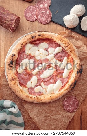On a rustic kitchen table, fresh Neapolitan pizza rests, topped with savory salami and creamy mozzarella. The artisan dough reflects the heart of Italian culinary artistry in a warm atmosphere