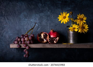 On The Rustic Wooden Shelf, A Bunch Of Grapes, Pomegranates And Yellow Jerusalem Artichoke Flowers. Still Life