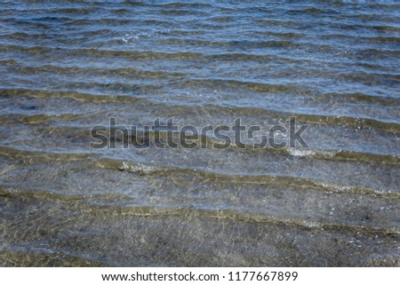 On a sandy shallow shore continuous small waves coming through the beach from the ocean on a bright sunny day.