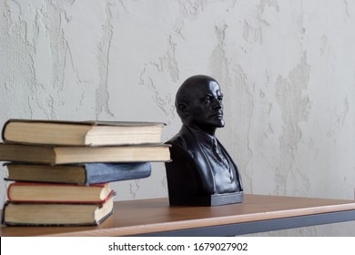 en una estantería hay un montón de libros viejos al lado de un busto de Lenin
