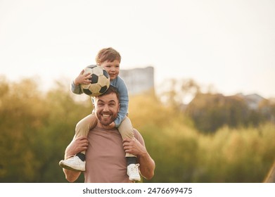 On shoulders, with soccer ball. Happy father with son are having fun on the field at summertime. - Powered by Shutterstock