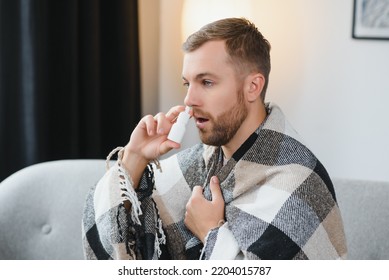 On Sick Leave. Ill Young Man Stay At Home On Workday Sneezing Feeling Bad Catching Cold Flu. Unhealthy Millennial Male Sitting On Sofa Blowing Nose At Paper Tissue Take Pills Medicine For Treatment