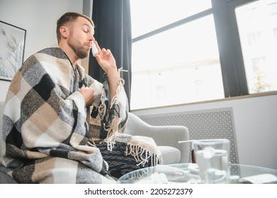 On Sick Leave. Ill Young Man Stay At Home On Workday Sneezing Feeling Bad Catching Cold Flu. Unhealthy Millennial Male Sitting On Sofa Blowing Nose At Paper Tissue Take Pills Medicine For Treatment