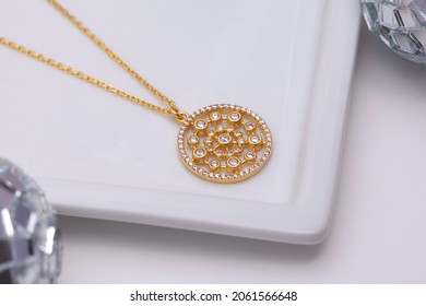 On A Soft White Background, A Gold Necklace On A White Plate And Disco Balls Around It.  Close Up.