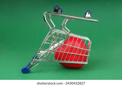 On a solid green background sits a small metal shopping cart with blue handles containing a red heart. The cart stands upside down, simulating disappointment with the purchase. - Powered by Shutterstock