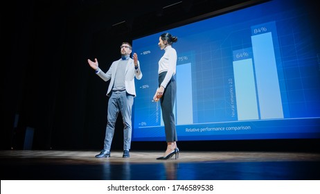 On Stage, Successful Female CEO And Male COO Speakers Present Company's New Product, Show Infographics, Statistics On Big Screen, Talk About Growth. Live Event, Tech Startup, Business Conference