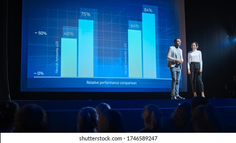 On Stage, Successful Female Executive And Male Manager Present New Product, Show Infographics, Statistics On Big Screen, Talk About Growth. Live Event, Tech Startup, Business Conference